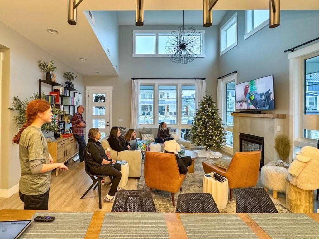 A spacious modern living room featuring a high ceiling, a large Christmas tree, and a group of people seated and conversing.