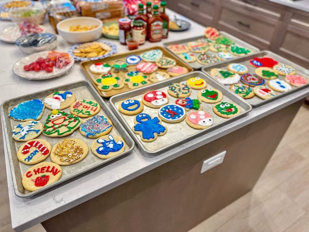 Trays of decorated Christmas cookies on a kitchen island topped with a collection of bowls, plates, and spices.