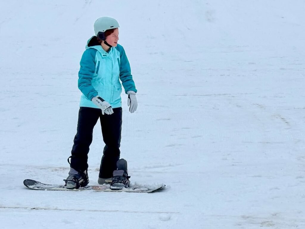 A person wearing a teal jacket and helmet is skiing on a snowy slope.