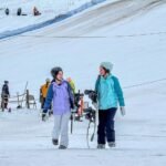 Christmas Eve Two individuals skiing on a snowy slope, enjoying a winter day with a scenic mountain backdrop.