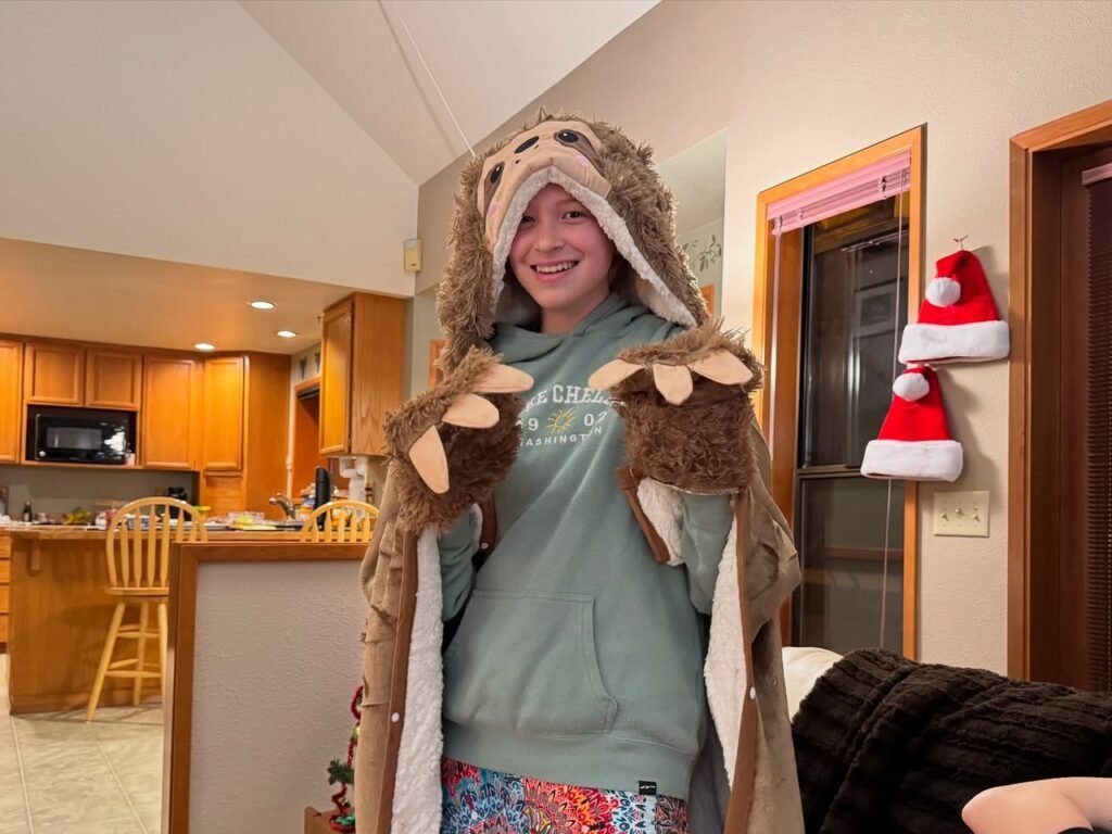 A smiling person wearing a playful animal costume in a bright kitchen decorated with Santa hat accents.