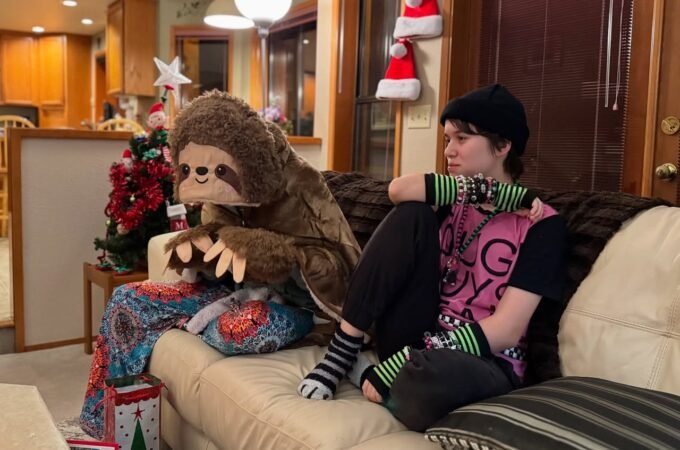 A person sitting on a couch in a festive room with a giant sloth pillow and Christmas decorations in the background.