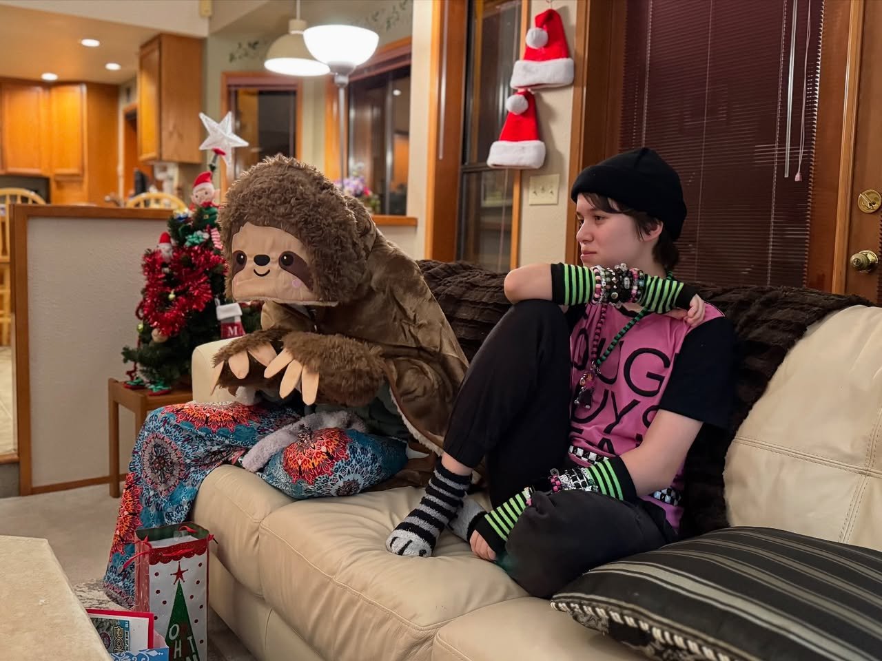 Christmas Eve A person sitting on a couch in a festive room with a giant sloth pillow and Christmas decorations in the background.