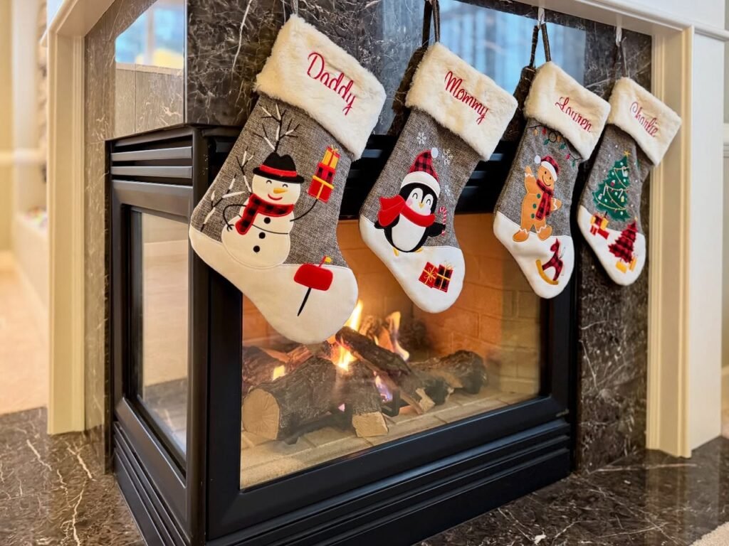 Four Christmas stockings with snowman and penguin designs hang above a modern fireplace.