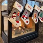 Christmas Eve Four Christmas stockings with snowman and penguin designs hang above a modern fireplace.