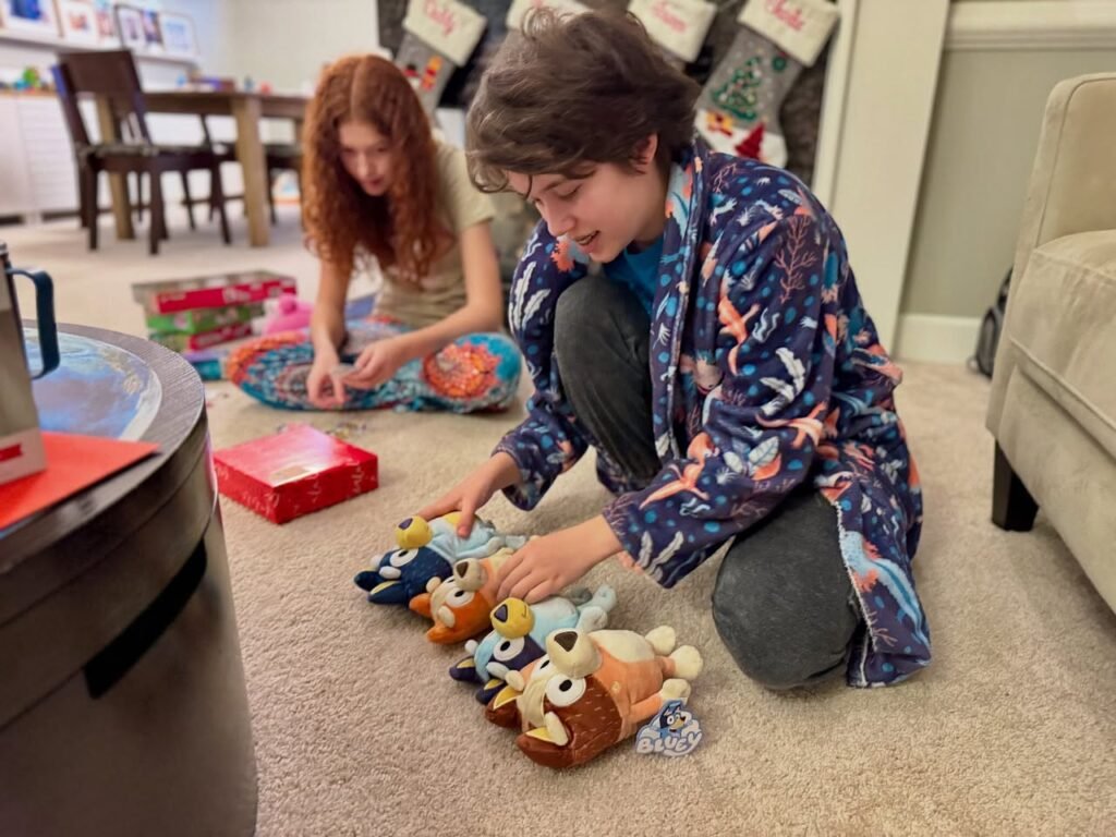 A person works with cuddly toys on the living room carpet next to a child drawing.