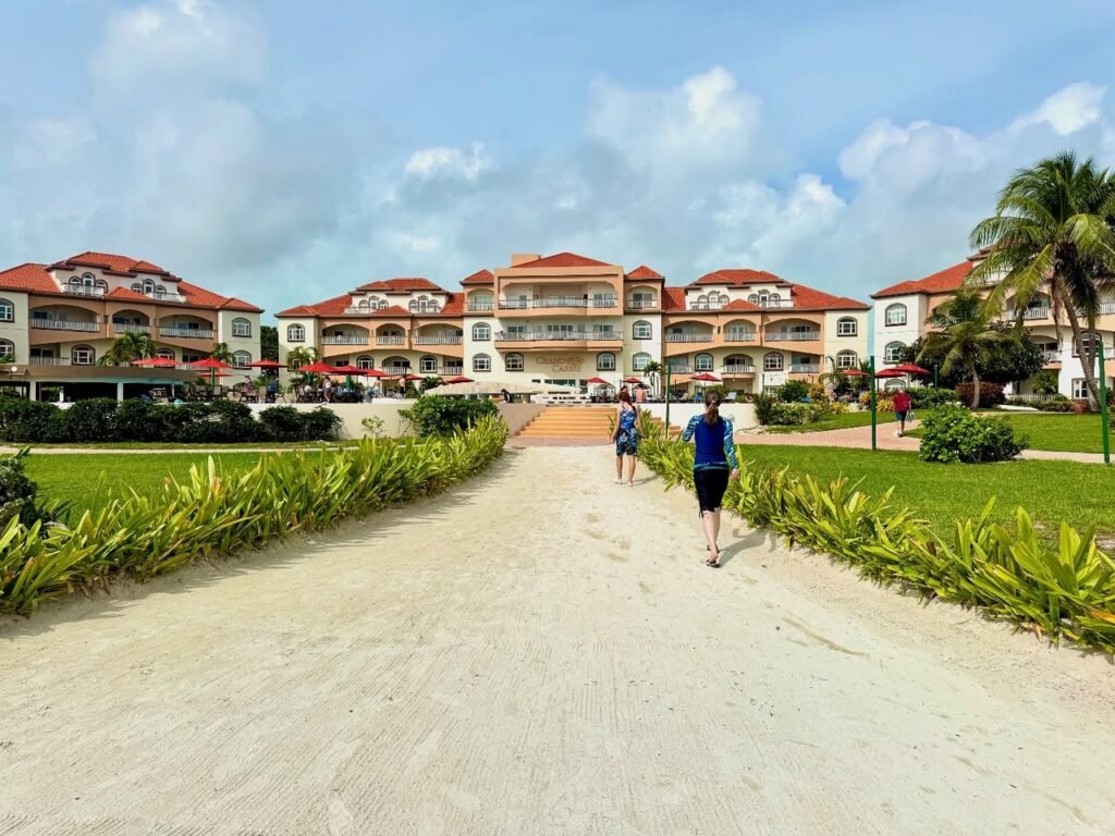 A sandy walkway lined with lush tropical plants leading to resort buildings.