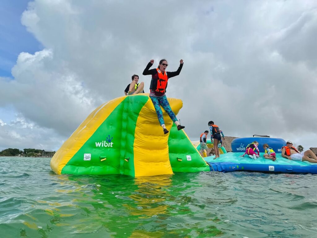 A colorful water slide in the ocean with people sliding down and floats nearby.
