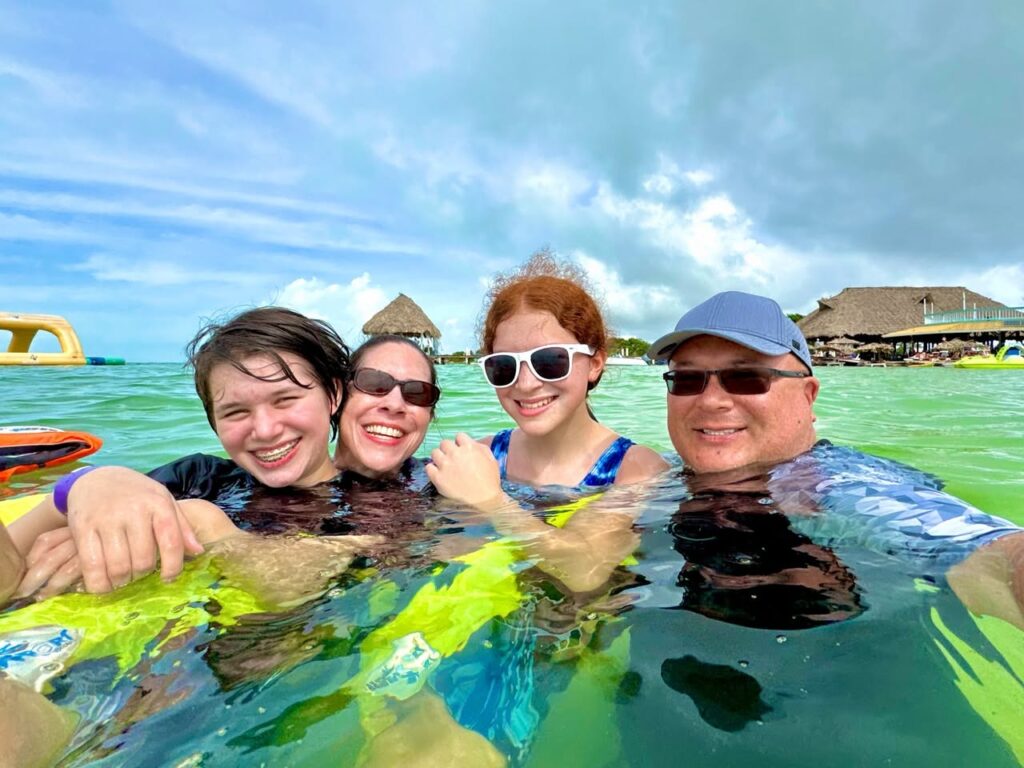 A happy group enjoys the warm, clear water of a tropical lagoon with overwater bungalows in the background.