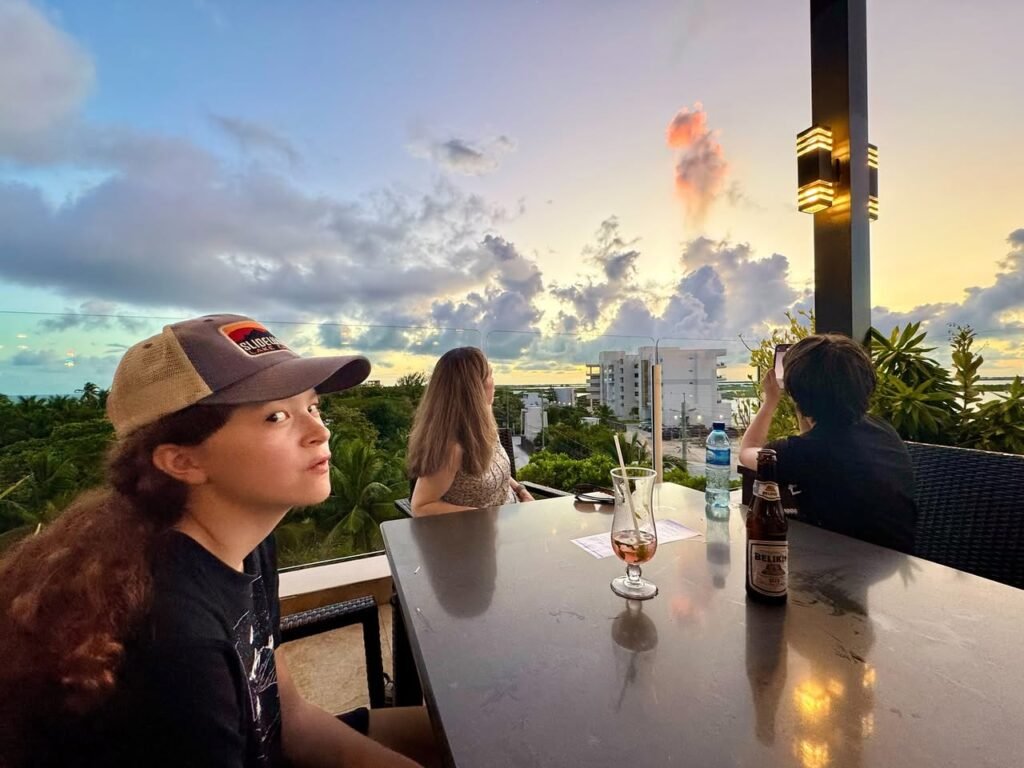 Friends enjoying cocktails at an outdoor bar while a large, colorful cloud formation shapes the sunset sky