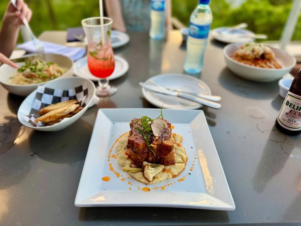A variety of dishes arranged on a table, including plate with meat, pasta, and fries, along with drinks.