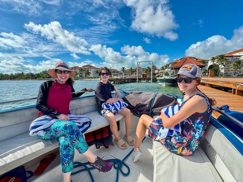A group enjoying a sunny day on a boat cruise by the water. Tropical buildings and a bright, cloudy sky frame the scene.