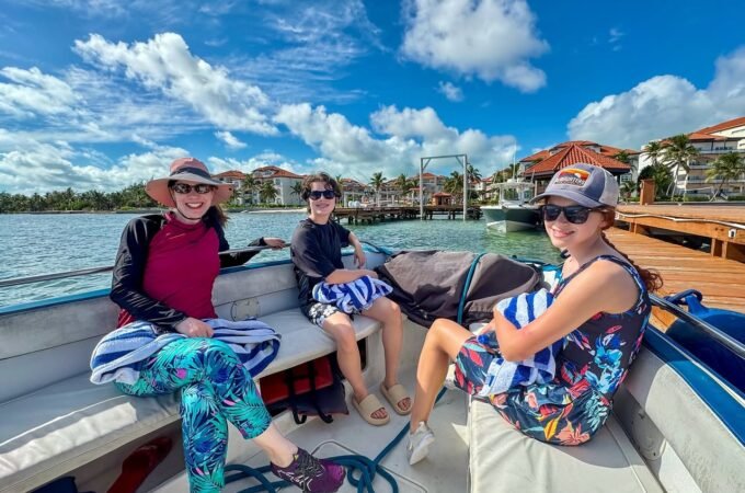 A group enjoying a sunny day on a boat cruise by the water. Tropical buildings and a bright, cloudy sky frame the scene.