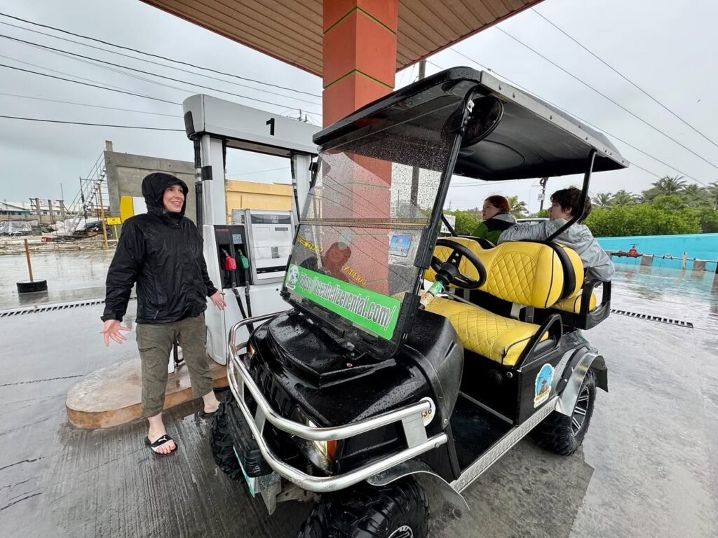A family stands next to a yellow and black utility vehicle at a gas station on a rainy day.