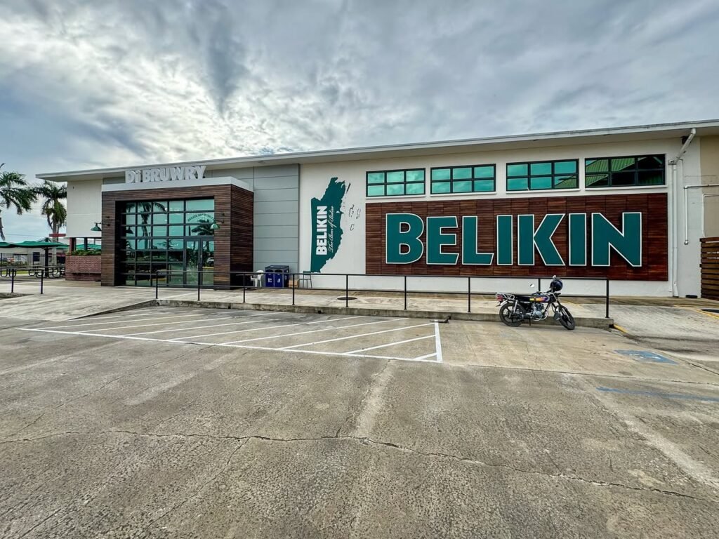 A white building with large BELIKIN branding on a red wall under a cloudy sky. A motorcycle is parked in the empty concrete lot.
