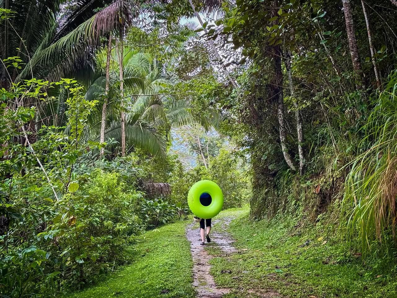 Tubing the Macal River A person walks away down a green jungle path holding a large neon green ring.