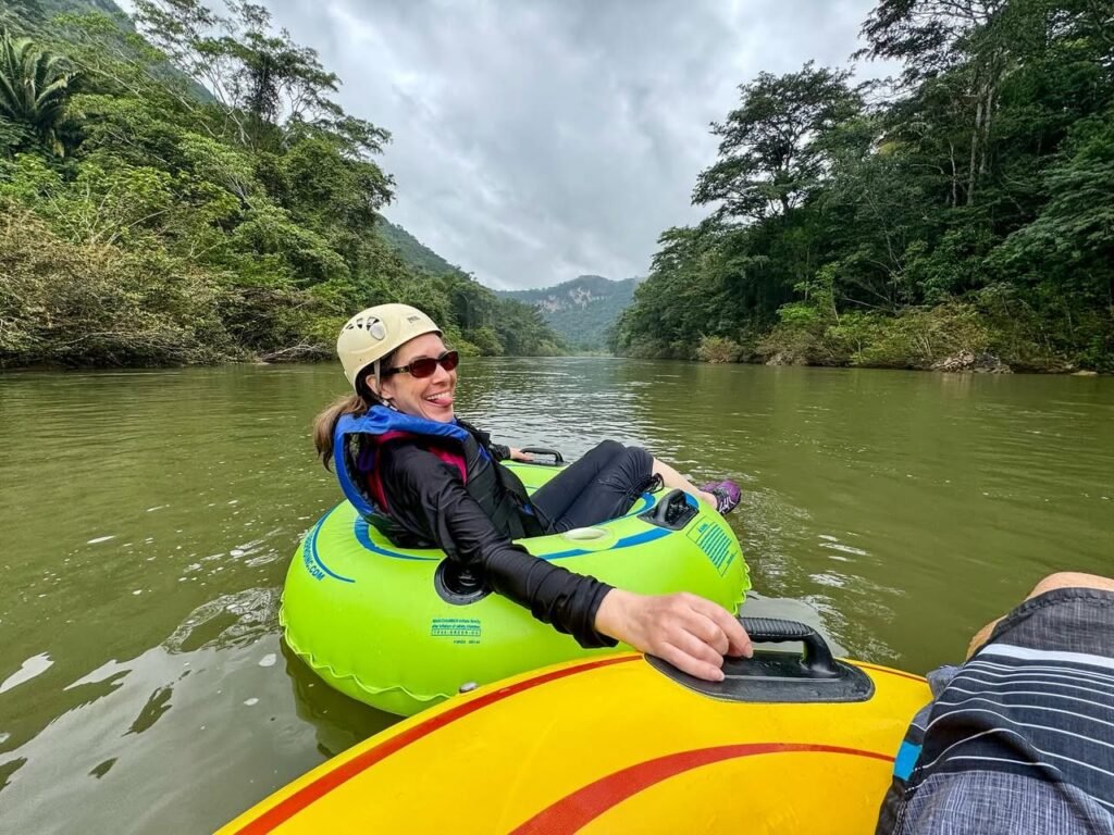 Relaxing on an inflatable tube while tubing a calm river surrounded by dense green jungle foliage.