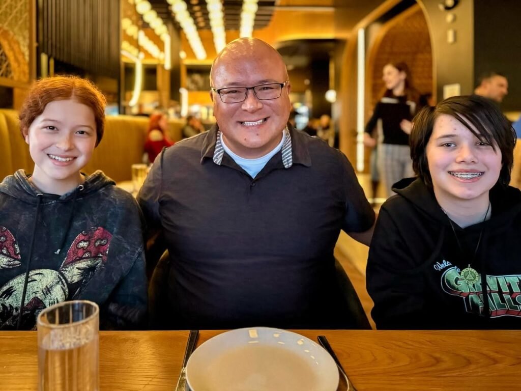 A family of three smiles for the camera during a dinner outing. The warm interior features modern decor and a bustling background.