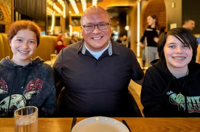 A family of three smiles for the camera during a dinner outing. The warm interior features modern decor and a bustling background.