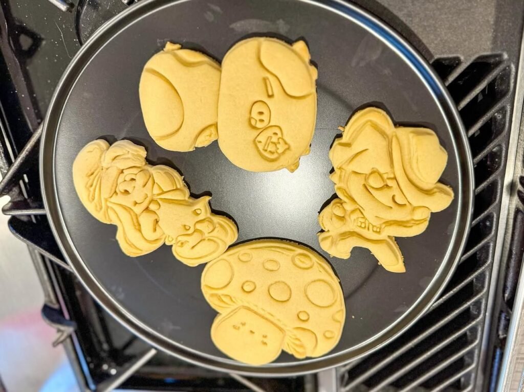 Different designs of pancakes baking in a frying pan.
