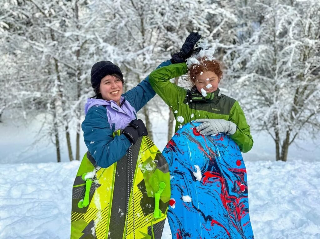 Two people holding snowboards in a snowy forest with snow-covered trees and ground.
