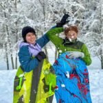 Two people holding snowboards in a snowy forest with snow-covered trees and ground.