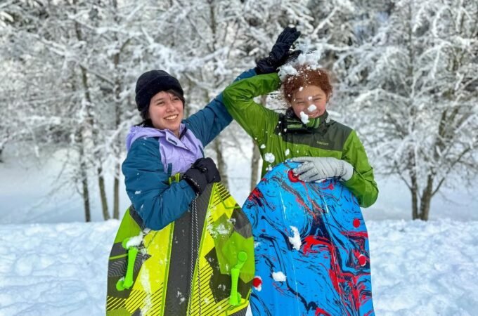 Two people holding snowboards in a snowy forest with snow-covered trees and ground.