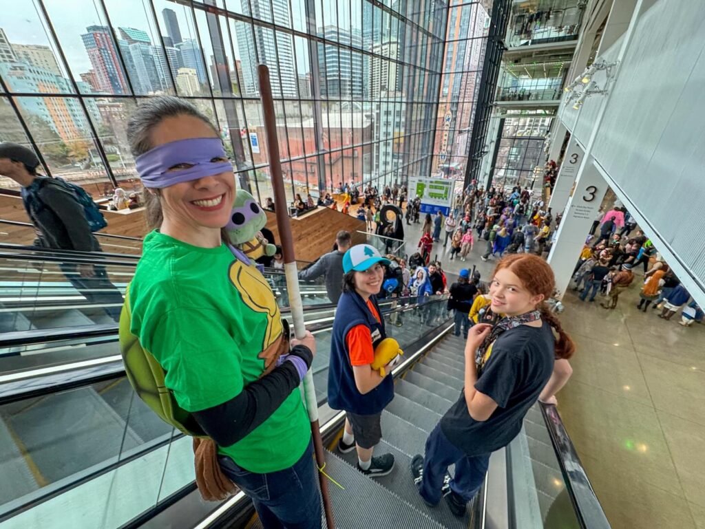 A group of people navigating an escalator inside a modern glass building, some wearing blindfolds, as part of an interactive experience.
