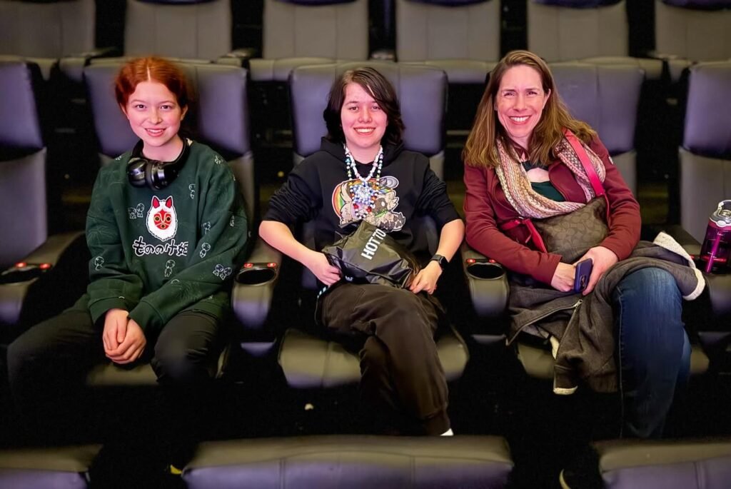 Three people sitting together in rows of theater seats. Close-up portraits of the individuals enjoying a night at the movies.