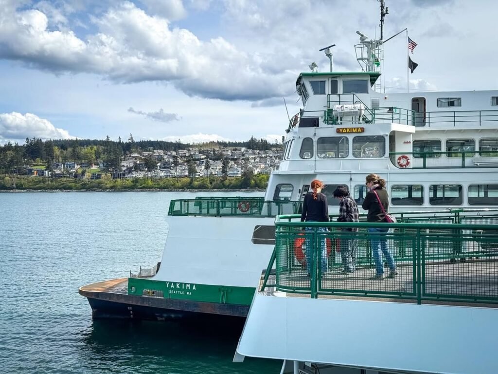 Travelers board a white and green ferry against a backdrop of coastal hills and California skies.
