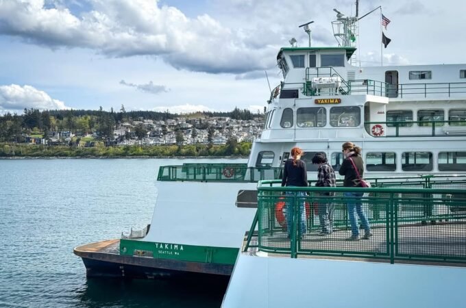 Travelers board a white and green ferry against a backdrop of coastal hills and California skies.