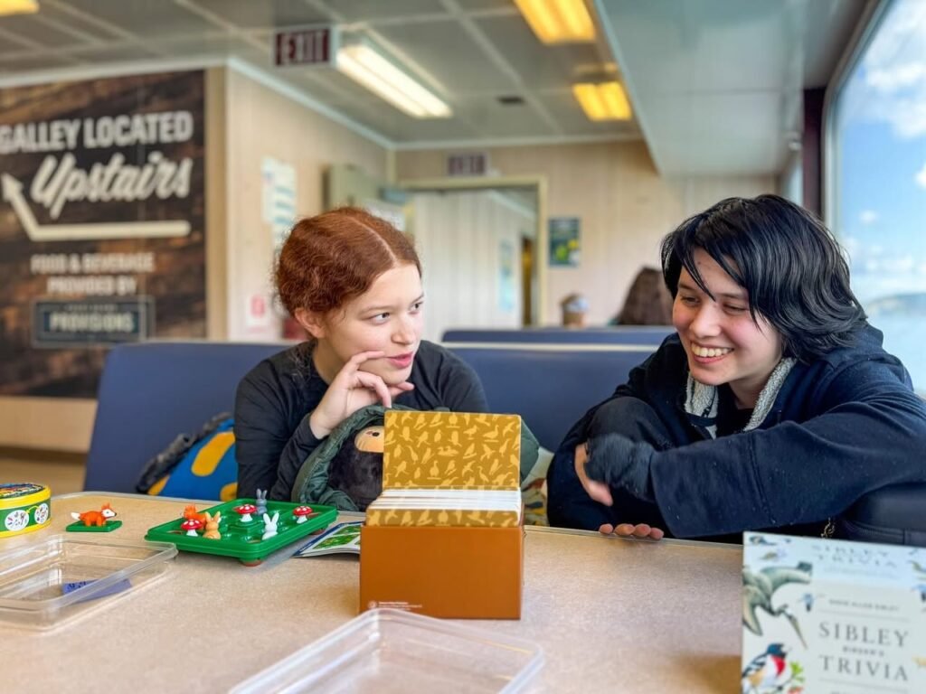 Two people playing a board game at an airport. The Sirley Trivia game box is visible in the background.