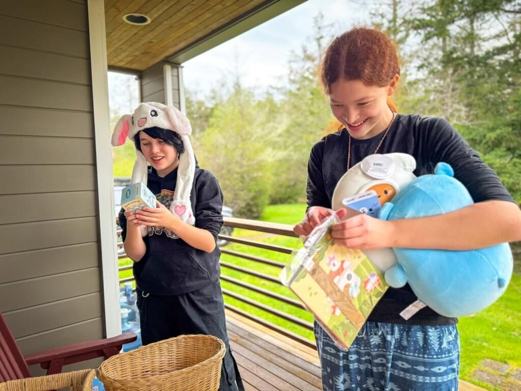 Two individuals enjoy a sunny Pacific Northwest porch with Easter gifts and plush toys. A basket and picture books are central to the scene.
