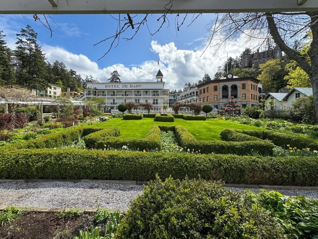 A picturesque view of a historic lodge surrounded by manicured formal gardens under a blue sky with clouds.