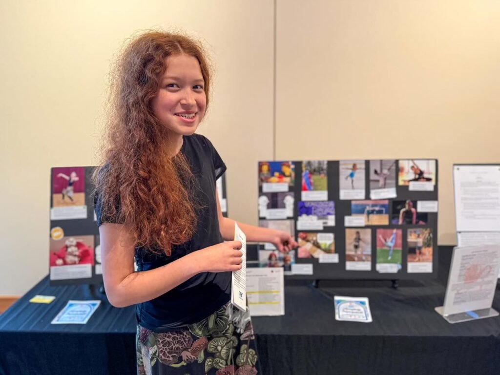 A young person stands beside a display of photographs and creative work on a black table.