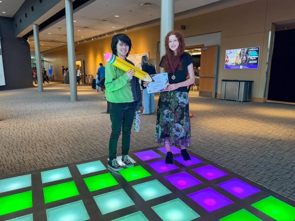 Two people standing on illuminated green and purple floor tiles inside a modern building.