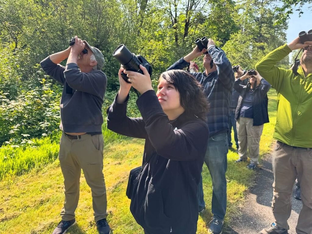 A group of people using binoculars and cameras to observe wildlife. Nature enthusiasts gather outdoors for wildlife viewing.