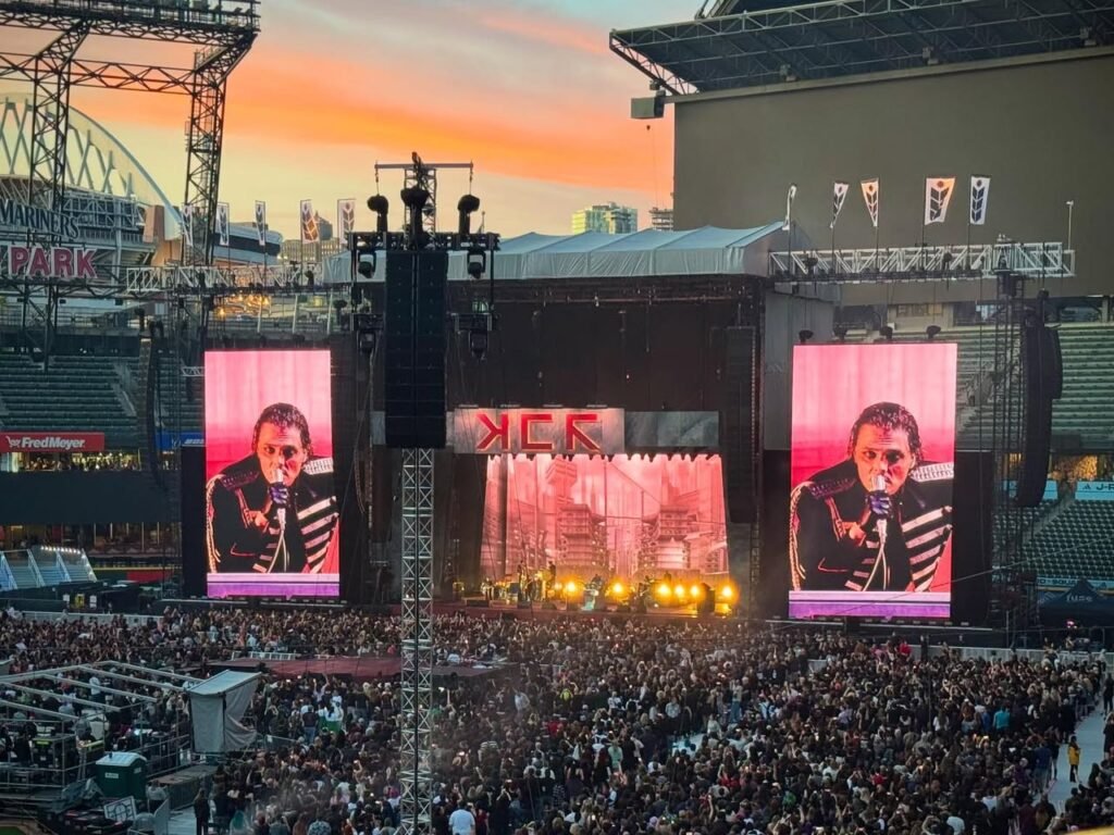 A singer performs under vibrant stage lights at a massive outdoor concert.