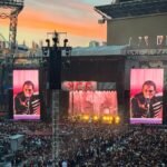 A singer performs under vibrant stage lights at a massive outdoor concert.