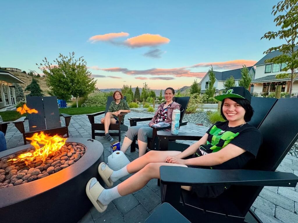 Neighbors relaxing on a patio with a burning fire pit and scenic mountain view at dusk.