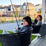Two people relaxing in black hanging patio chairs on a wooden deck surrounded by well-maintained urban homes.