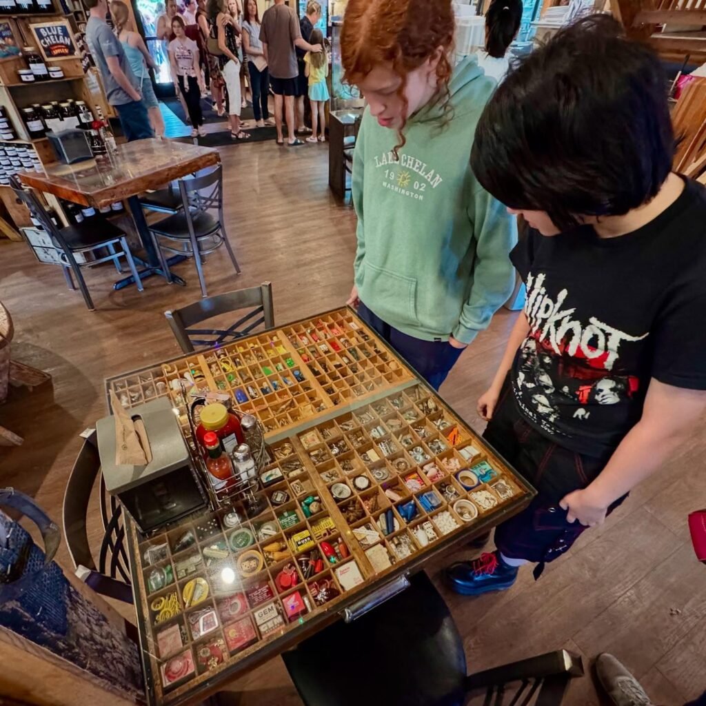 Two people examine an extensive collection of vintage buttons displayed on a table at a local shop or marketplace.