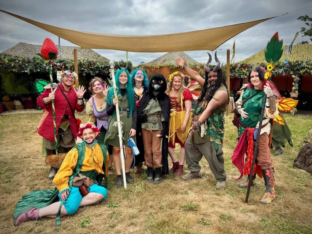 A group of costumed garden gnomo performers poses together on a grassy field under a canopy. The costumes are colorful and whimsical, matching characters from Mary Poppins.