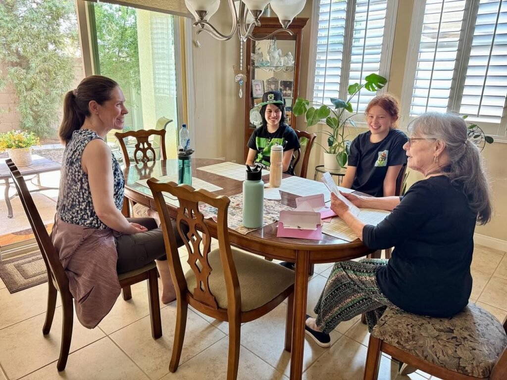 A multi-generational family enjoys lunch together at a wooden table in a sunlit dining room. Close-up shots highlight family members and the indoor greenery.