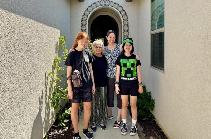 Four people posing in front of Spanish architecture with a decorative arched doorway and greenery.