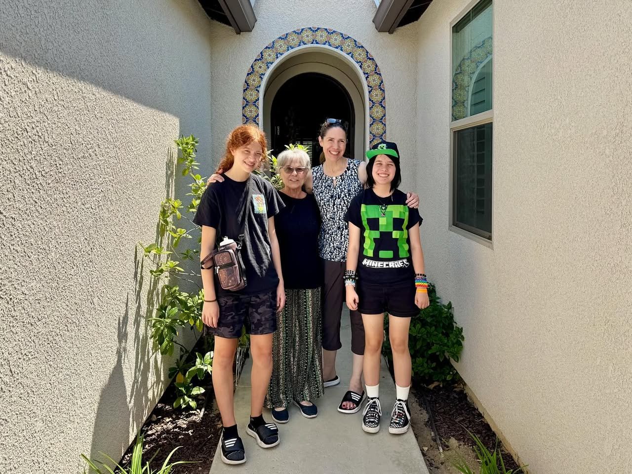 Four people posing in front of Spanish architecture with a decorative arched doorway and greenery.