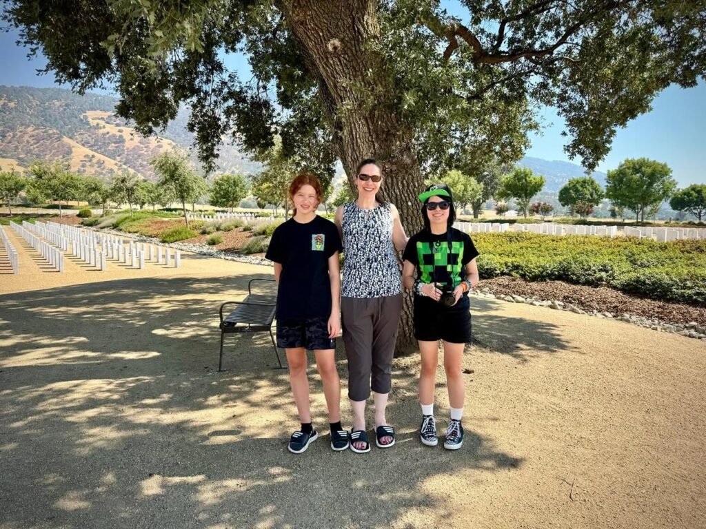 A group of people posing under a tree with mountains and a park in the background.