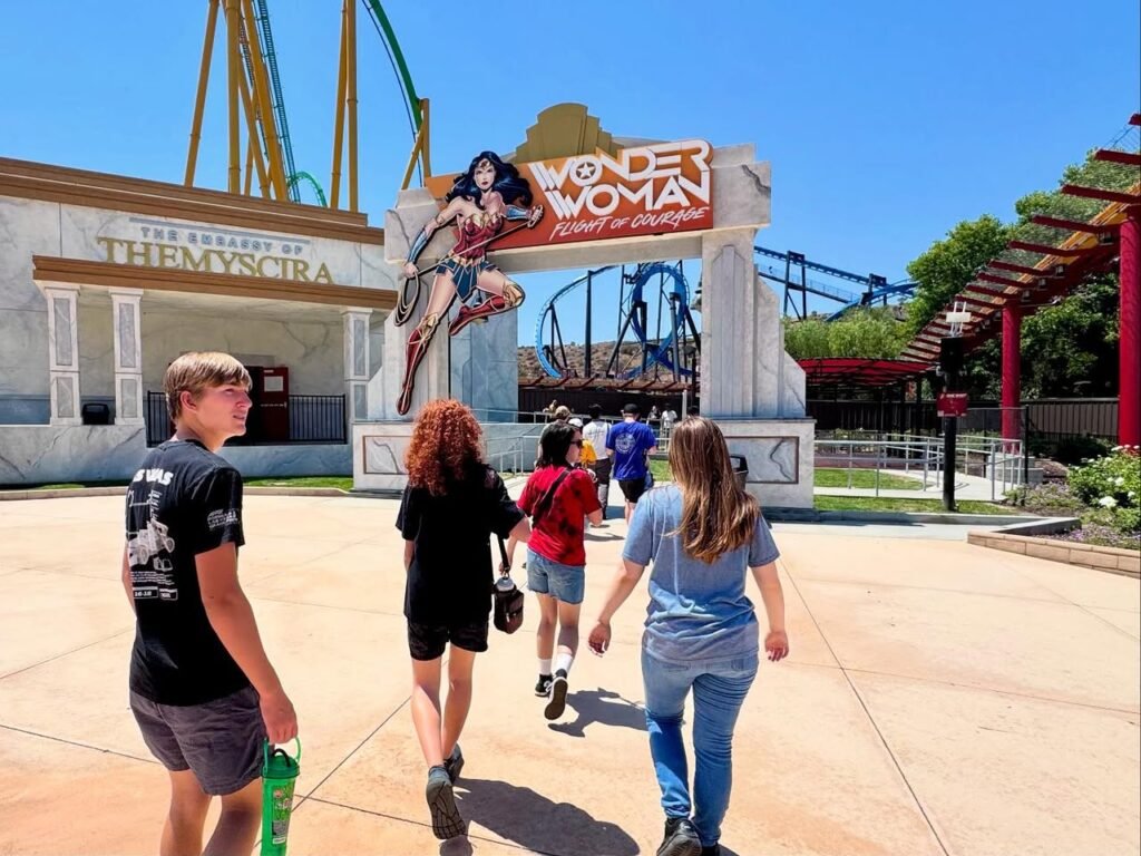 Visitors enjoy the Wonder Woman and Themyscira attractions at a sunny outdoor amusement park.