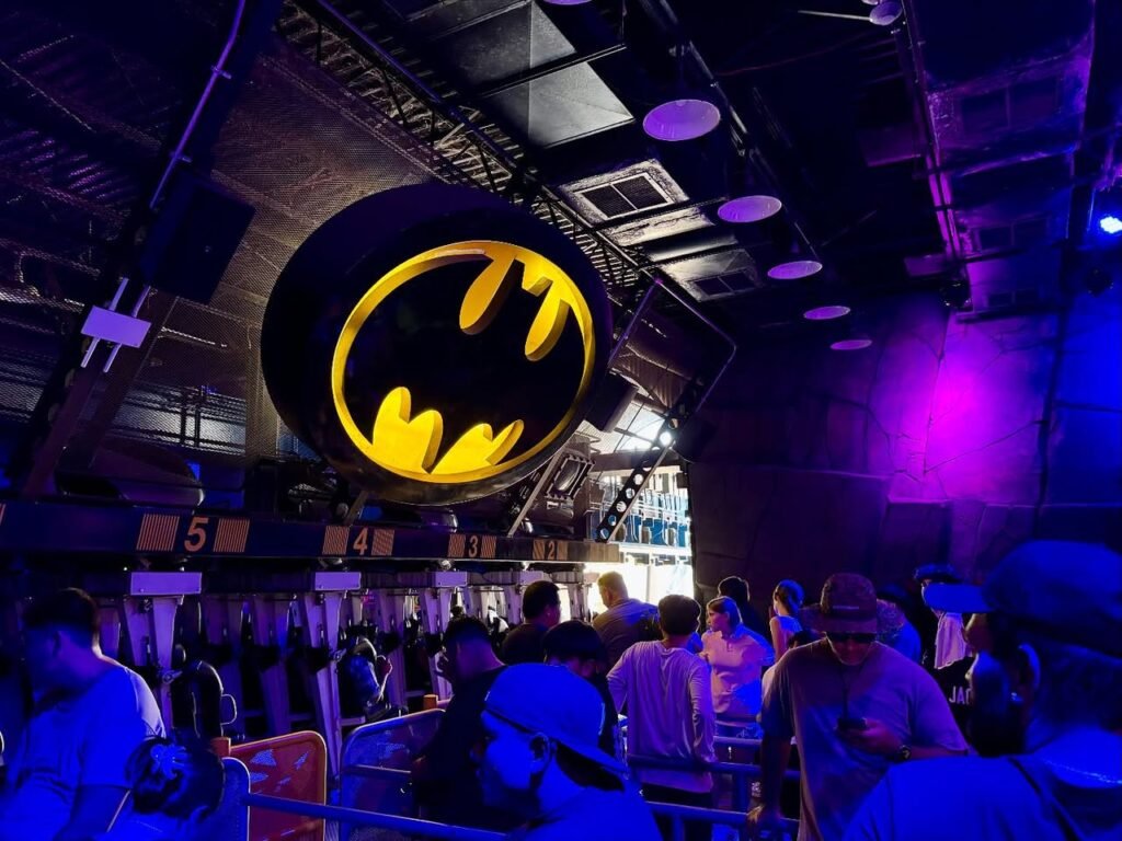A scene inside a Batman-themed amusement ride featuring a glowing bat symbol and riders in a darkened section.