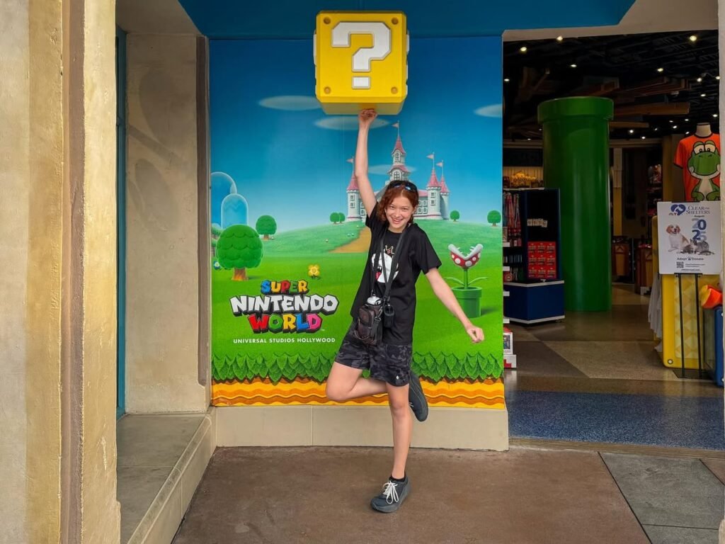 A visitor poses playfully in front of a Super Mario World themed photo backdrop featuring a question block.